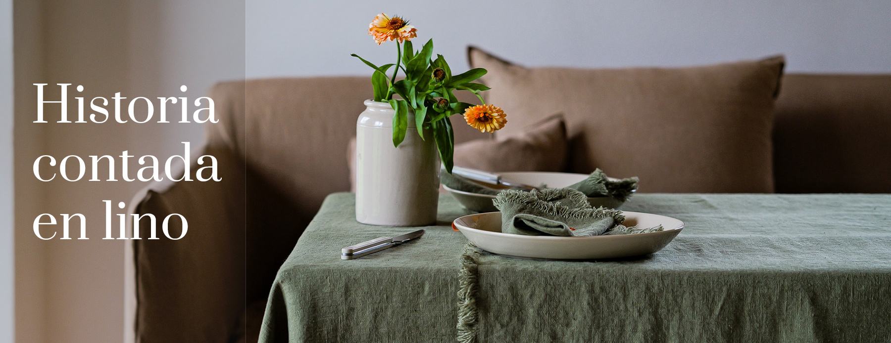Historia contada en lino – mantel verde con servilletas y flores de otoño frente a un sofá.